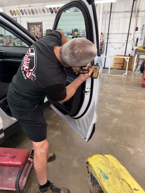 Mechanic repairing car door, using a tool. In a garage setting.