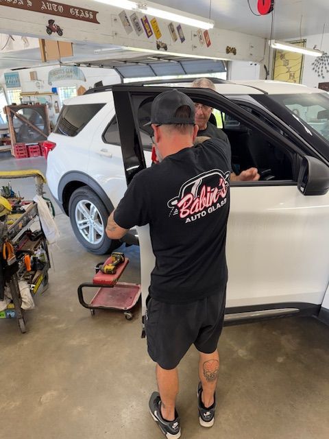 Two people installing a car window in a garage. One holds the window, the other assists.