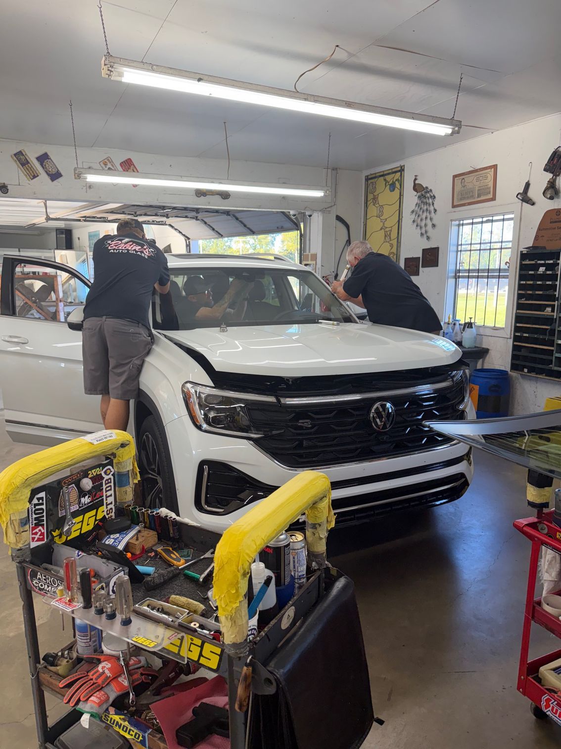 Two people installing a windshield on a white Volkswagen in a garage.