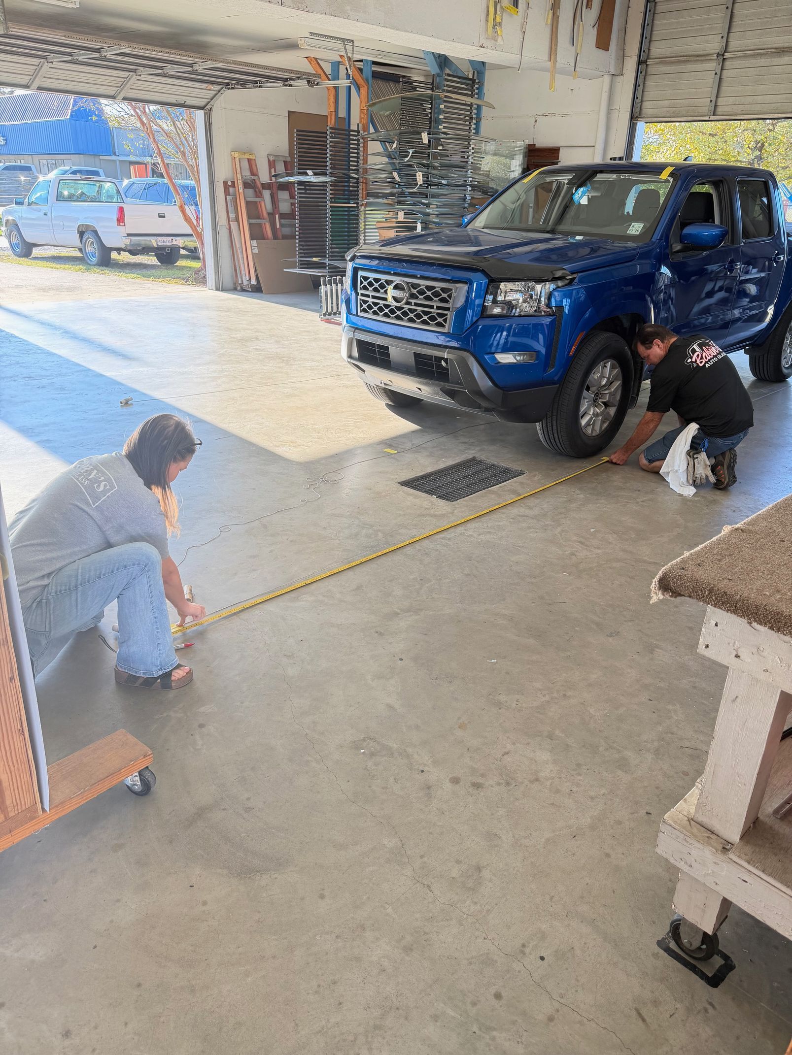 Two people measure a garage floor near a blue truck.