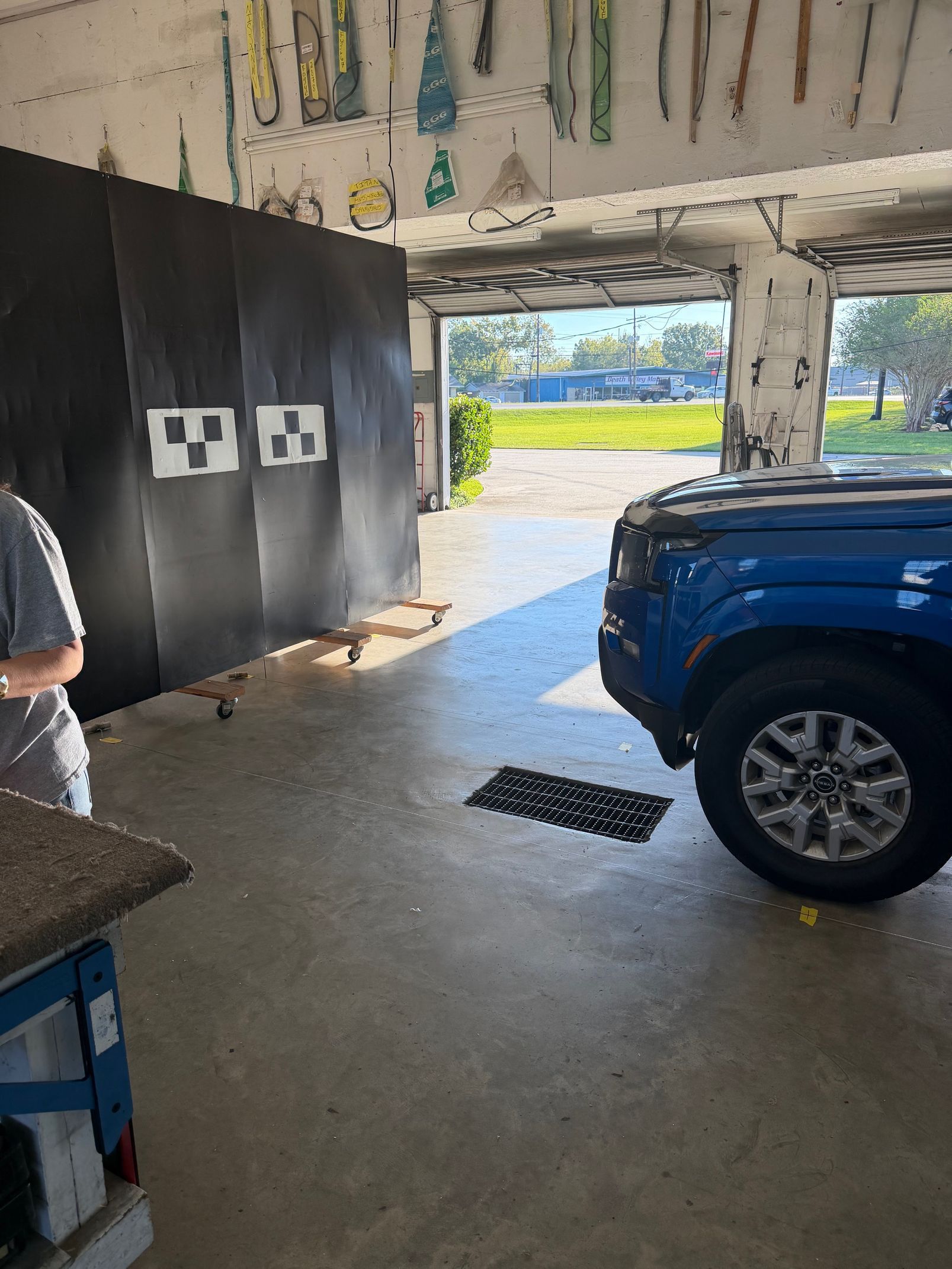 Blue car in a garage with black backdrop and checkered targets. Person stands near.