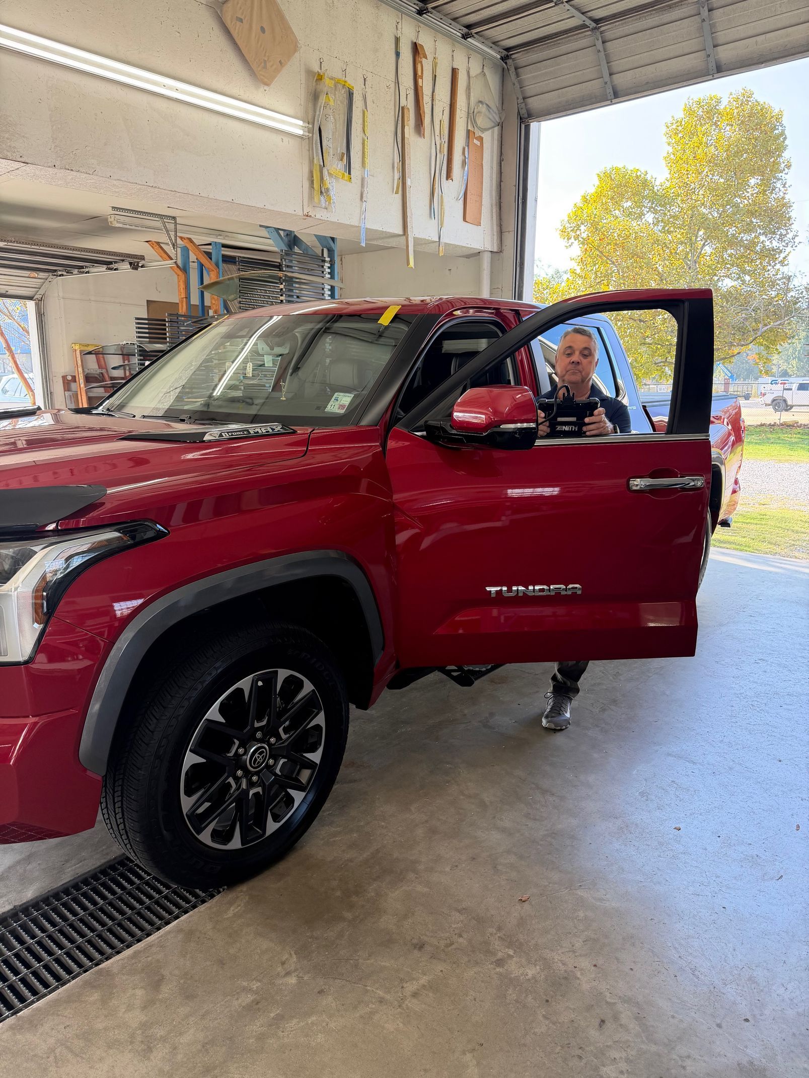 Red Toyota Tundra truck with open door; person inside gives a thumbs up in a garage.