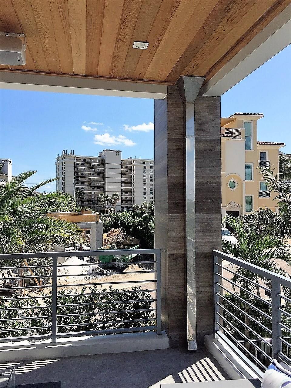 Balcony overlooking a cityscape with a modern building with wood ceiling, stone pillar, and metal railing.