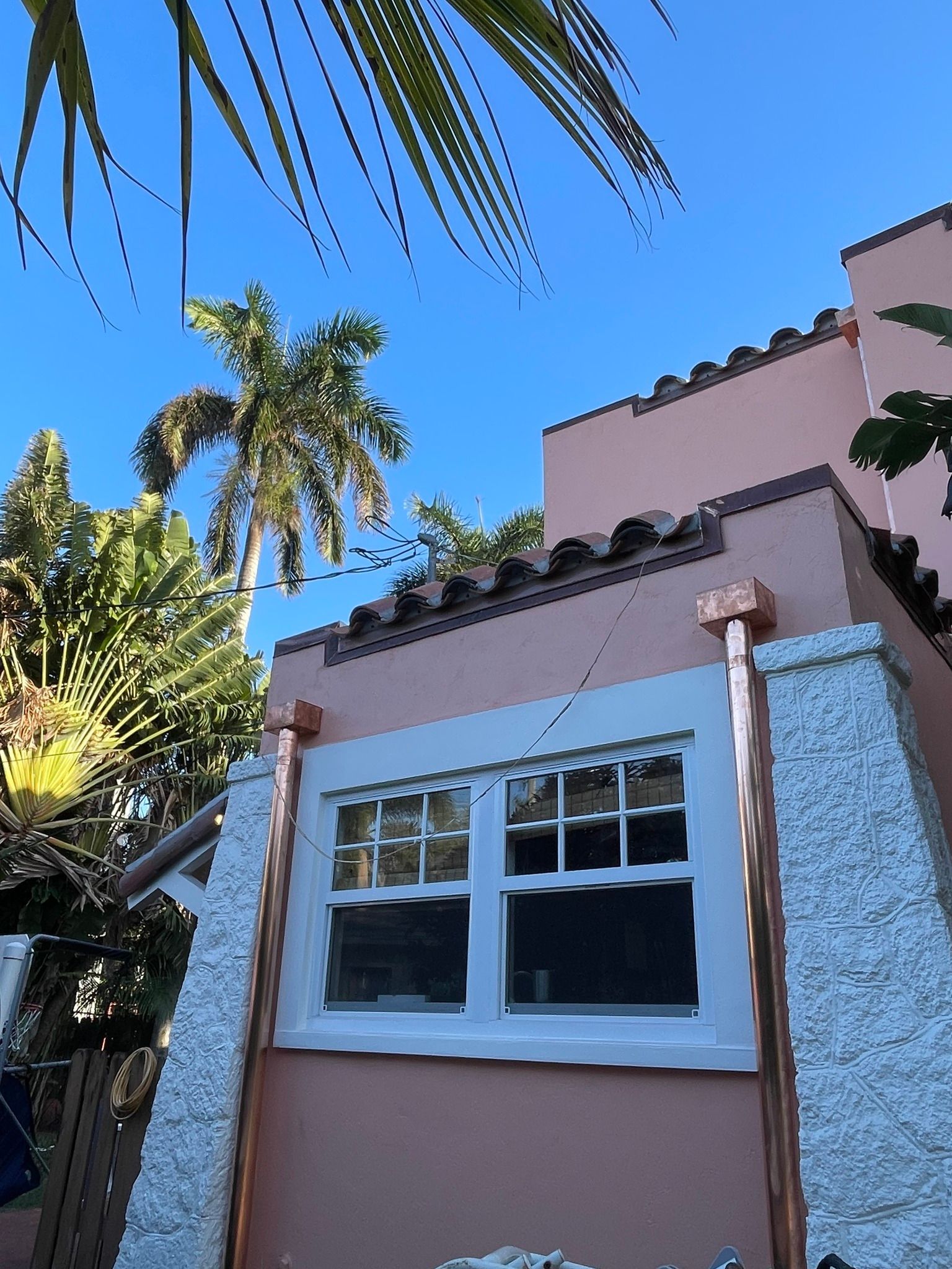 Pink stucco building with white-framed windows and copper accents under a bright blue sky, with palm trees visible.