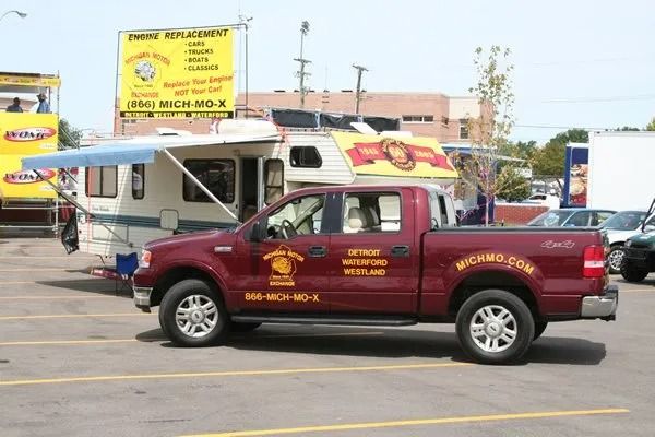 Red truck towing a camper in a parking lot, business signage visible.