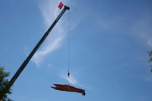 A crane lifting an orange boat against a clear blue sky.