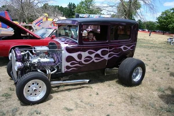 Purple hot rod with silver flames, parked on grass at an outdoor car show.