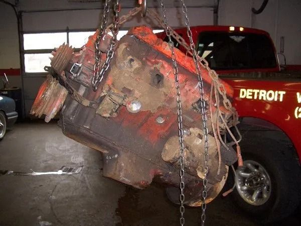 Engine block suspended by chains in a Detroit garage, painted orange.