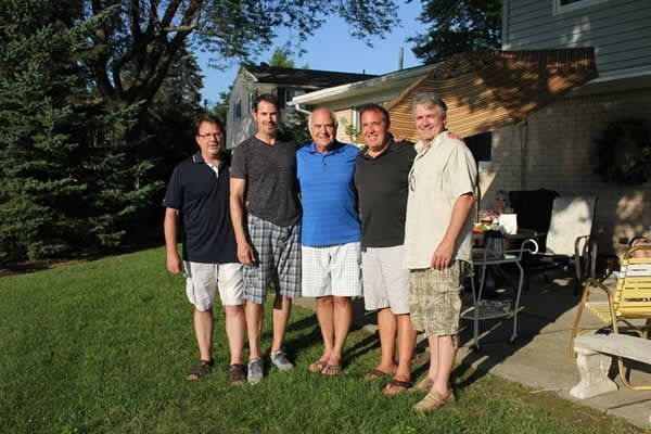 Five men standing together outdoors in front of a house, smiling.