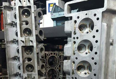 Three engine cylinder heads, possibly aluminum, showing valve and port details in a workshop setting.