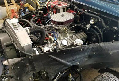 Engine compartment of a blue vehicle. Silver engine, radiator, and wiring visible. Black hoses and air filter.