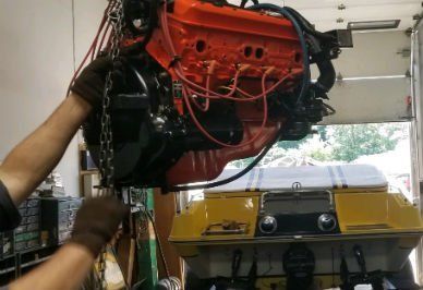 Engine being lowered into a yellow boat. Red engine, black chain, inside garage.