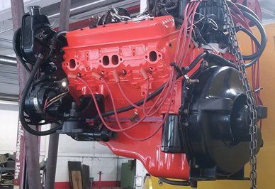 Red and black painted V8 engine hoisted in a repair shop.