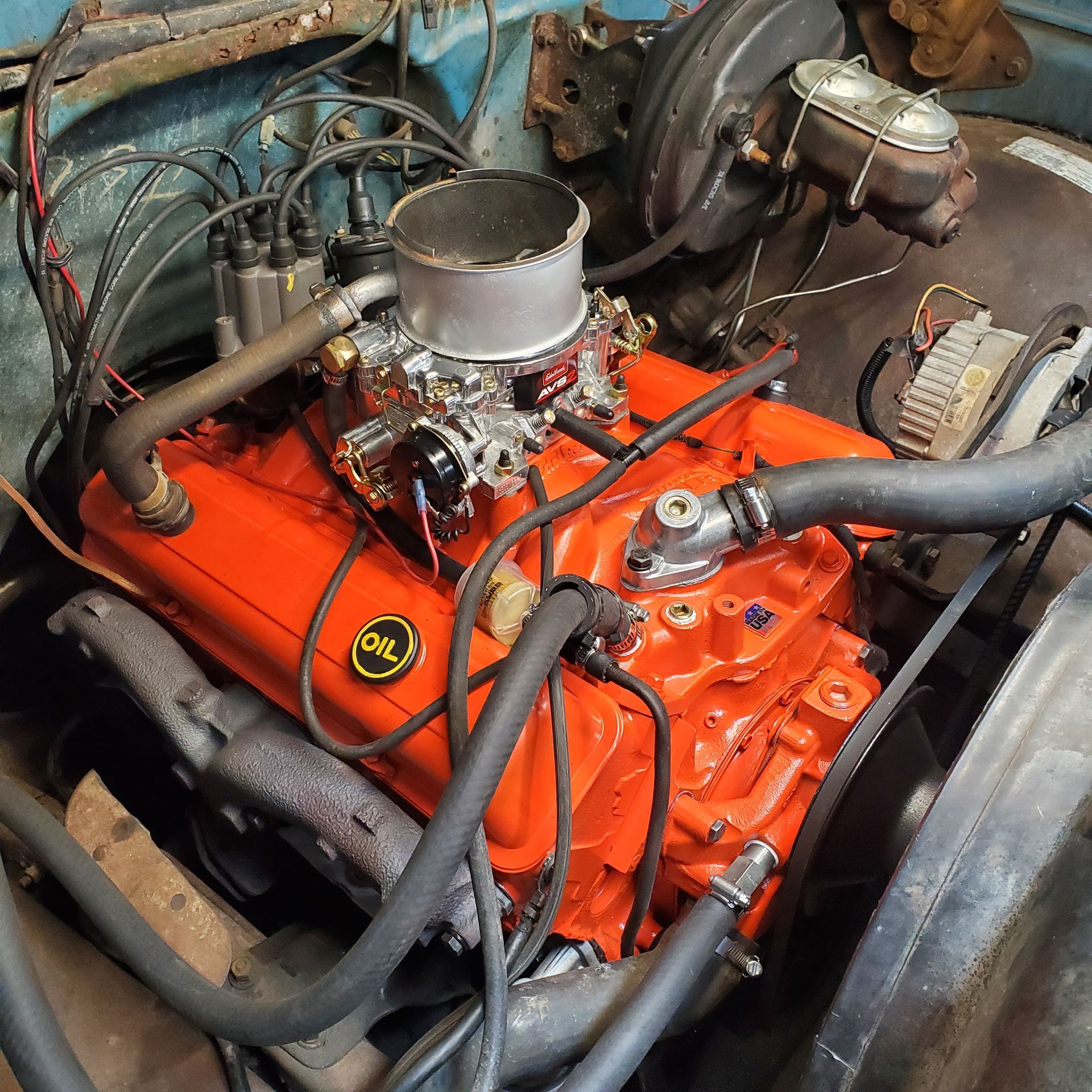 Orange engine in a vehicle with black tubes, a distributor, and carburetor.