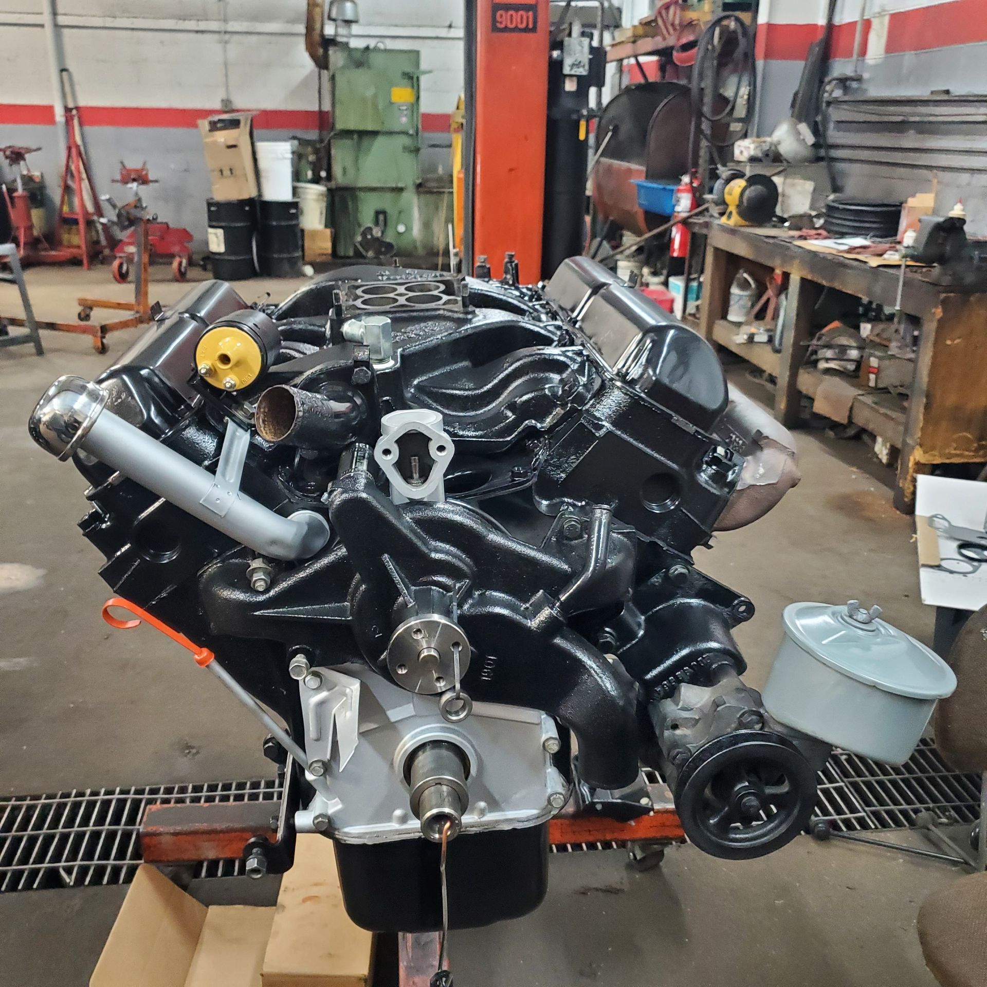 Black engine with silver components sits on a stand in a garage.