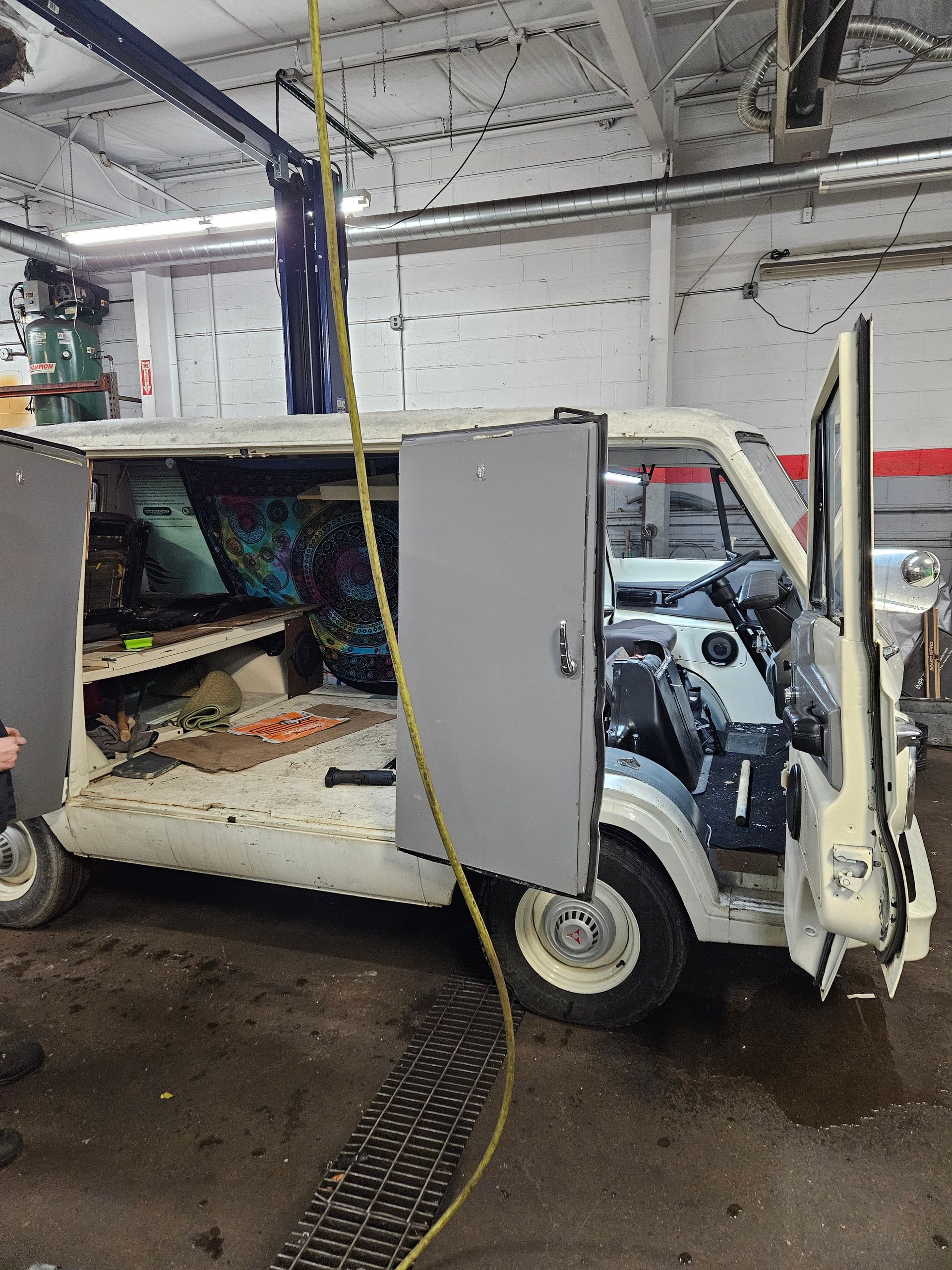 White van with open doors in a garage, undergoing repair. Interior is exposed with tools visible.