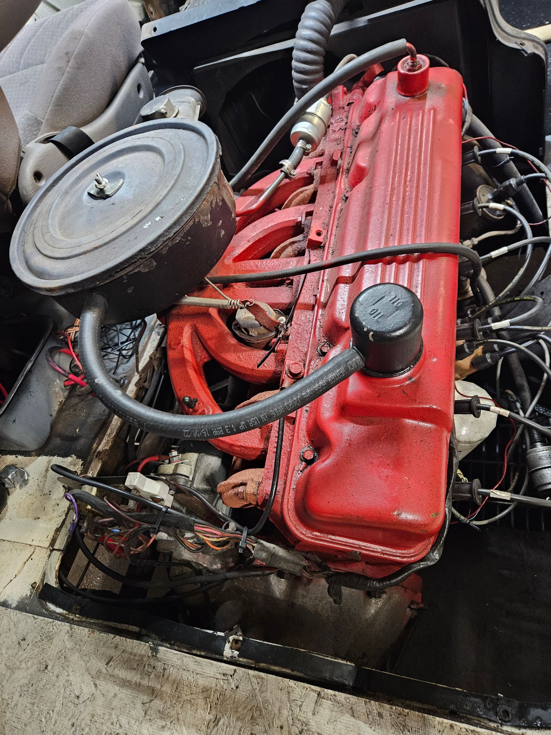 Red engine in a vehicle. It has a round air filter and many wires.