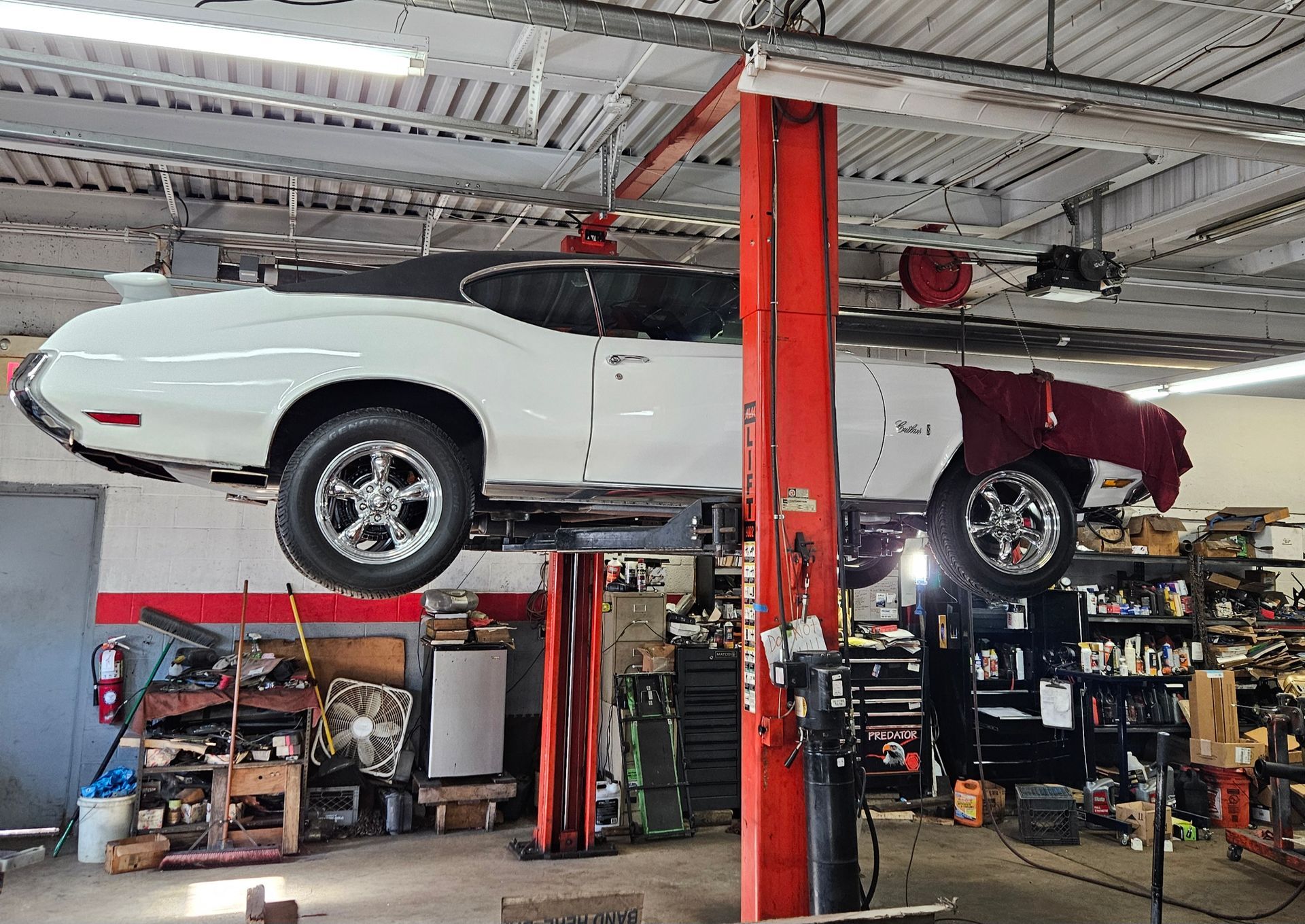 White and maroon classic car on a lift in a garage, undergoing repair.