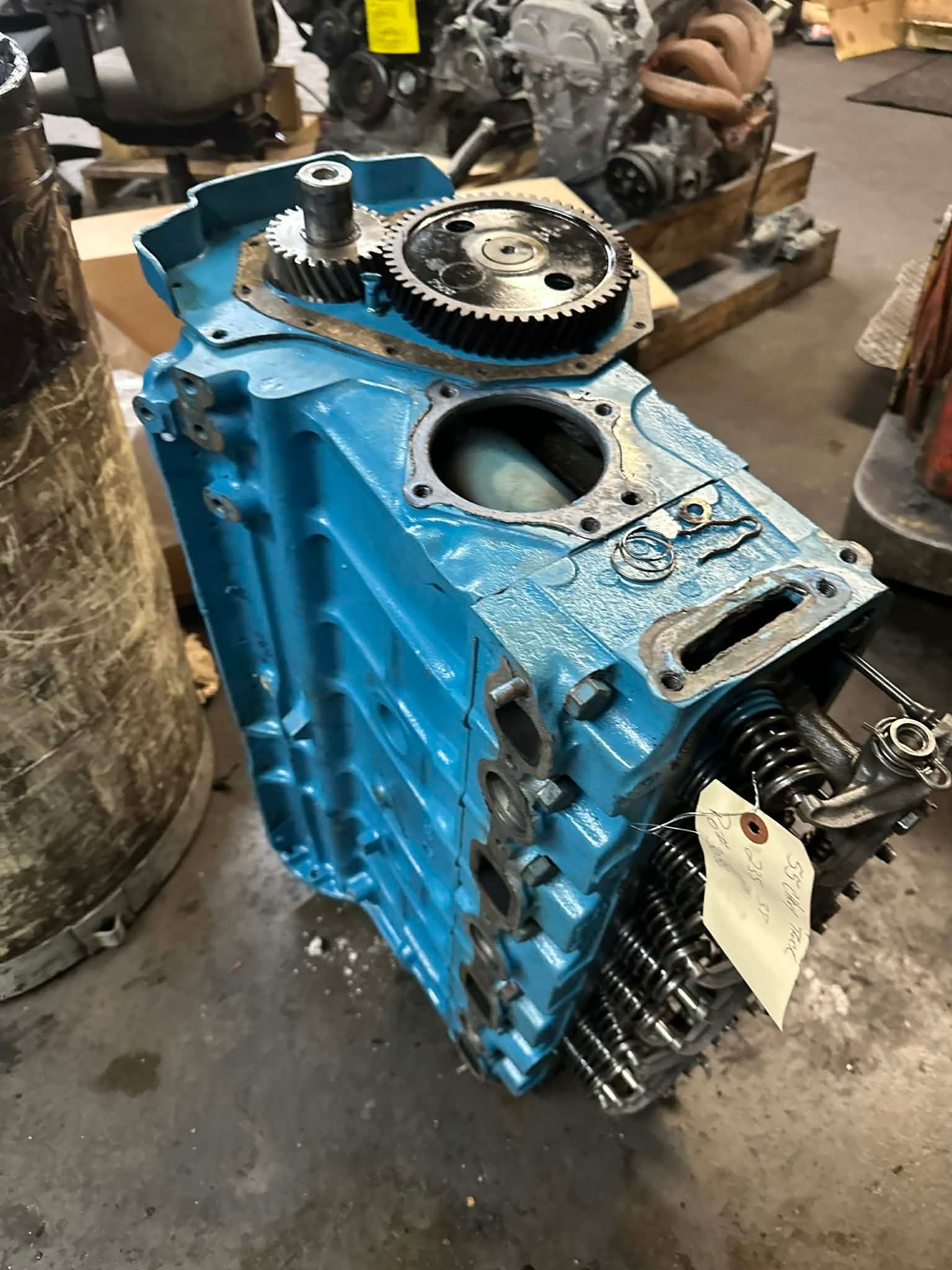 Blue engine block with gears and other parts on a shop floor.