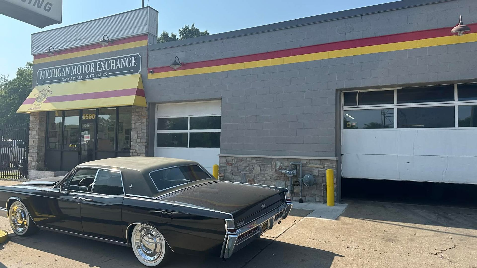 Black classic car parked in front of a gray auto shop with open garage door.