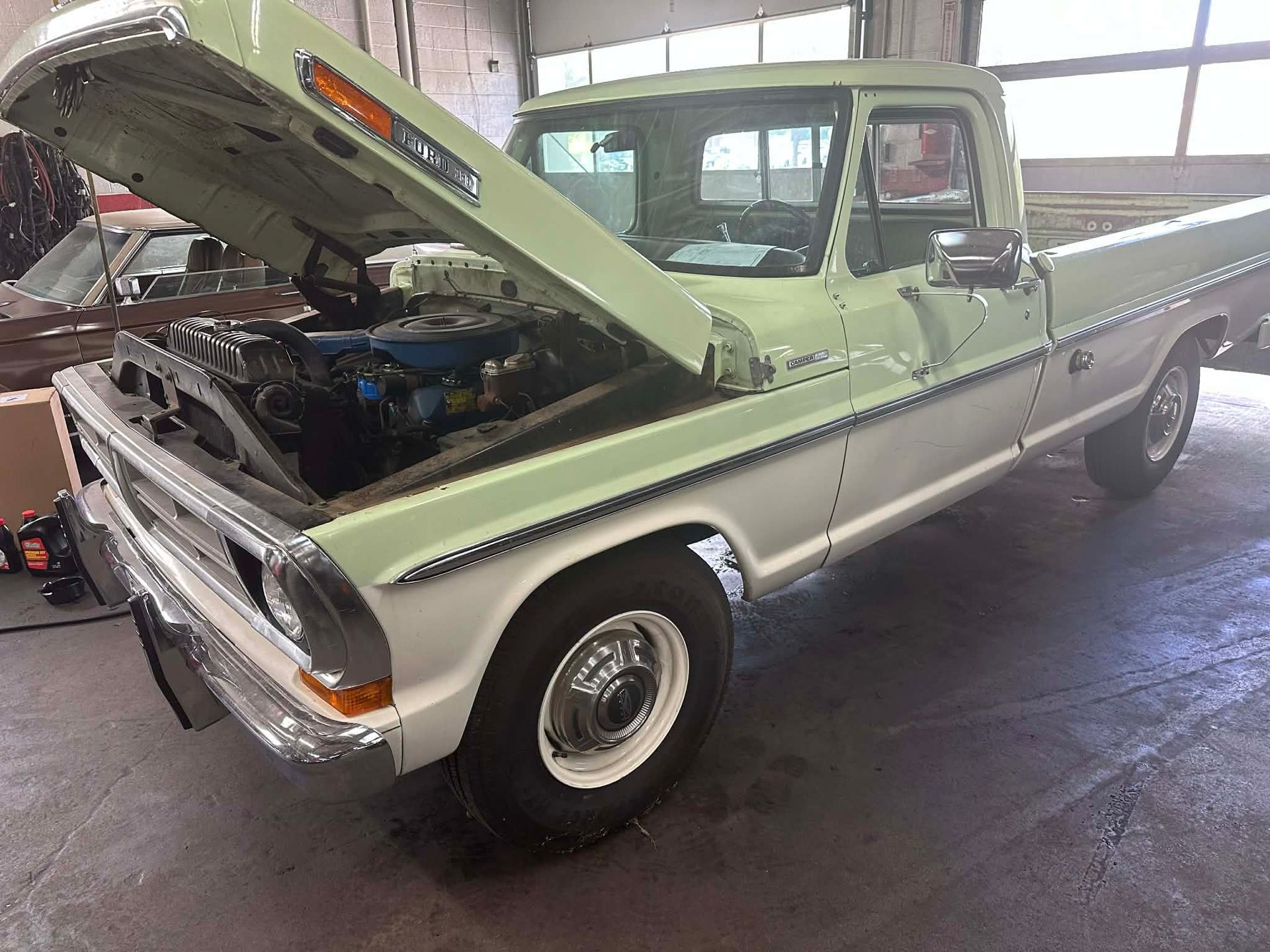 Green and white vintage Ford pickup truck with hood open in a garage.