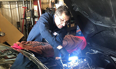 A man is working on a car with the hood open in a garage.