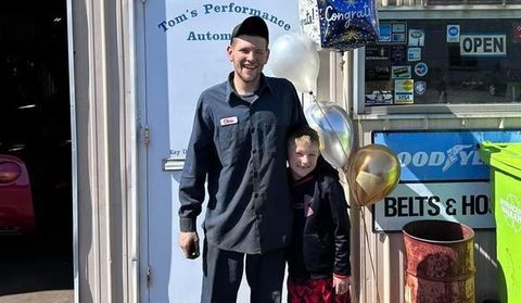 A man and a boy are standing in front of a goodyear sign