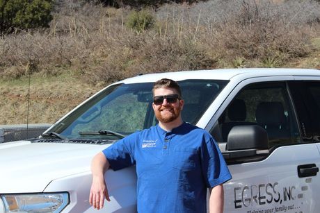 A man in a blue shirt is leaning against a white truck.