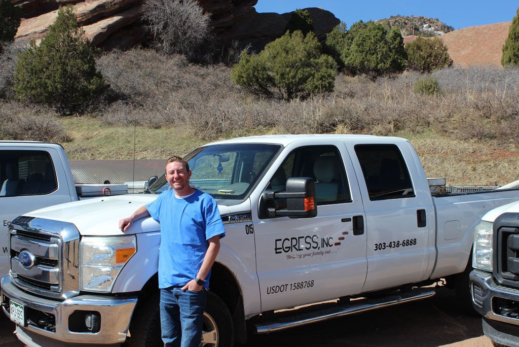 A man in a blue shirt is standing in front of a pickup truck.