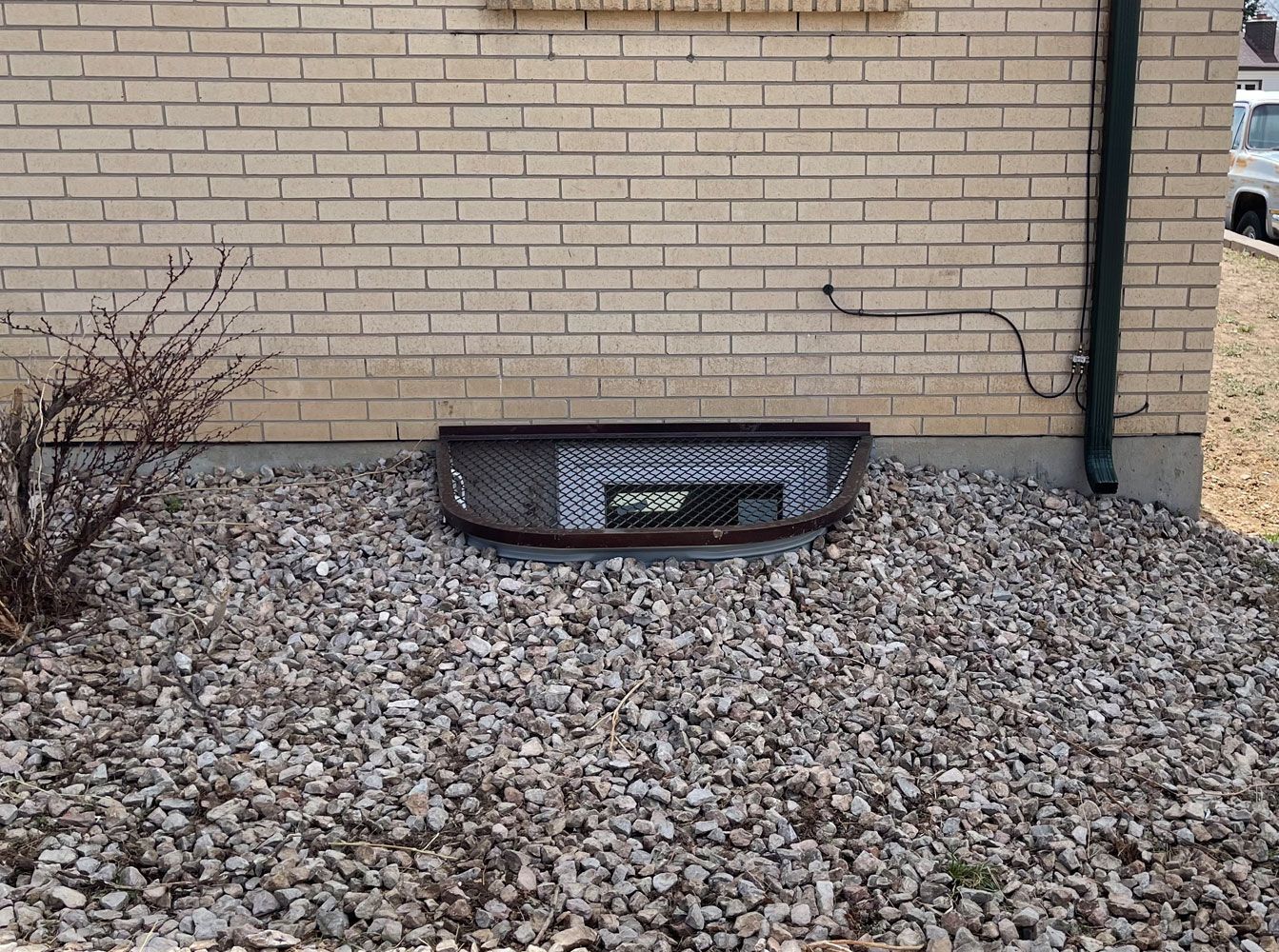 A window well in the side of a brick building surrounded by gravel.
