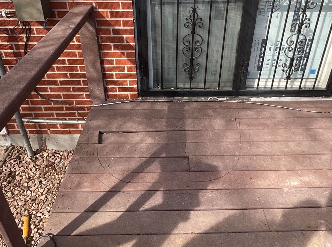 A wooden deck with a metal railing is in front of a brick building.