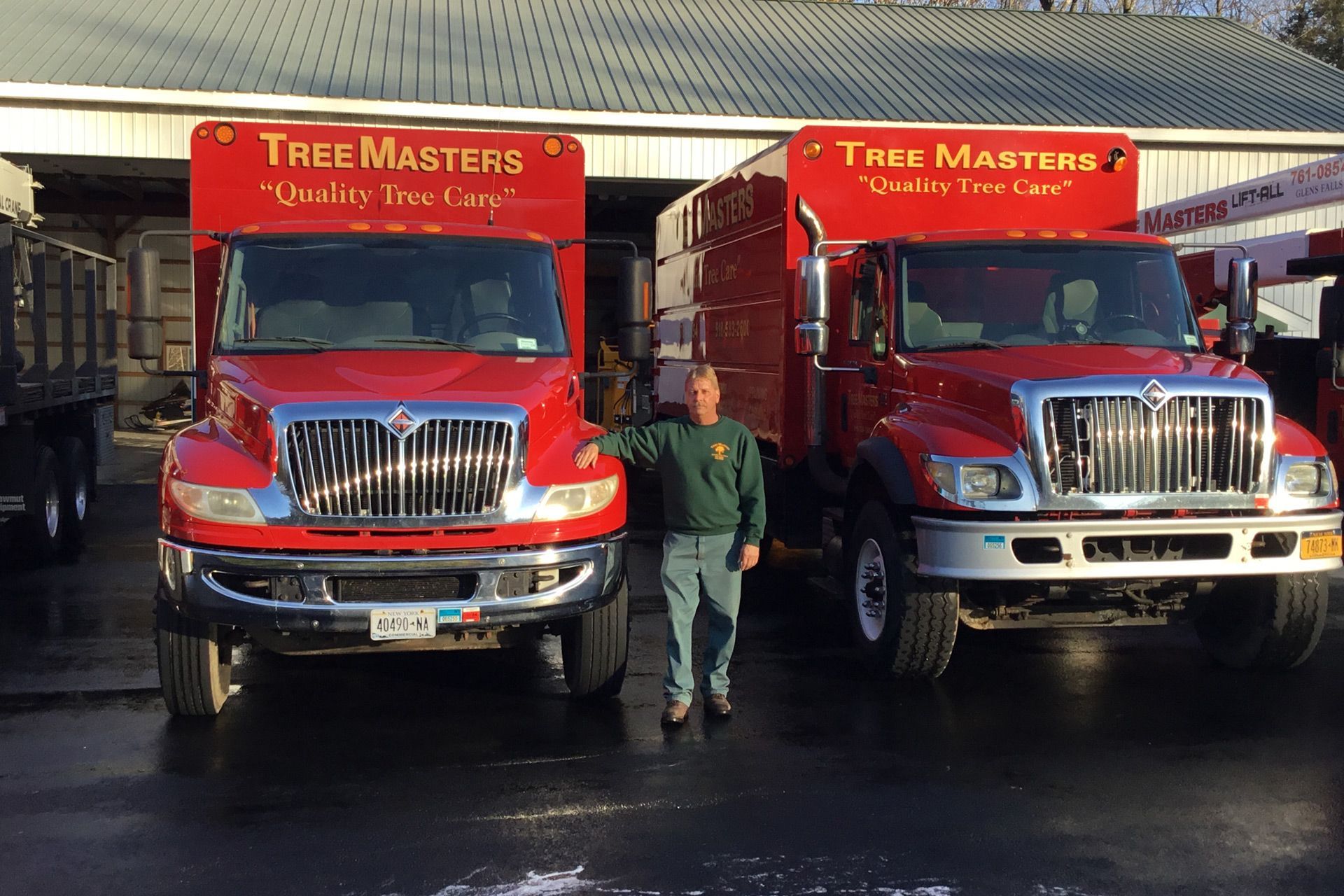 A man is standing in front of two red trucks that say tree masters
