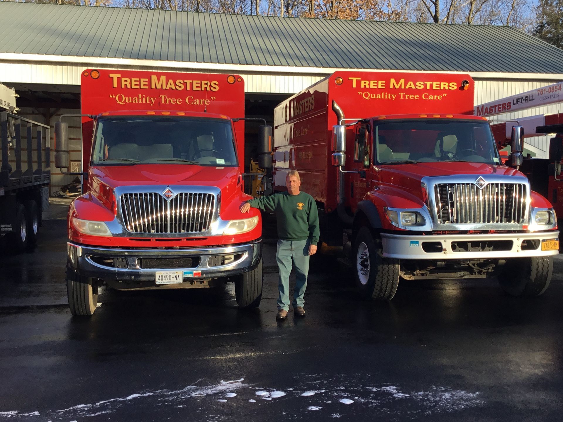 A man stands in front of two red tree masters trucks