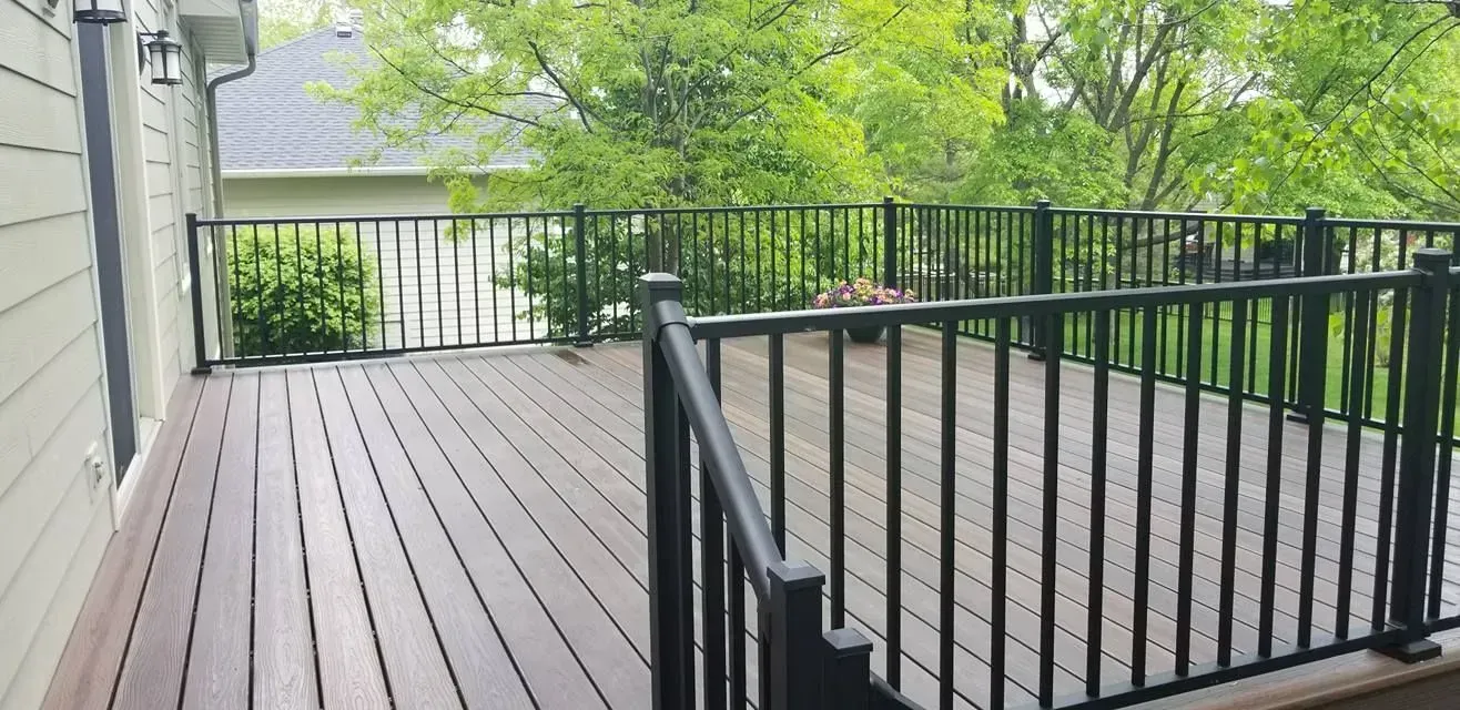 A wooden deck with a black railing and a house in the background.