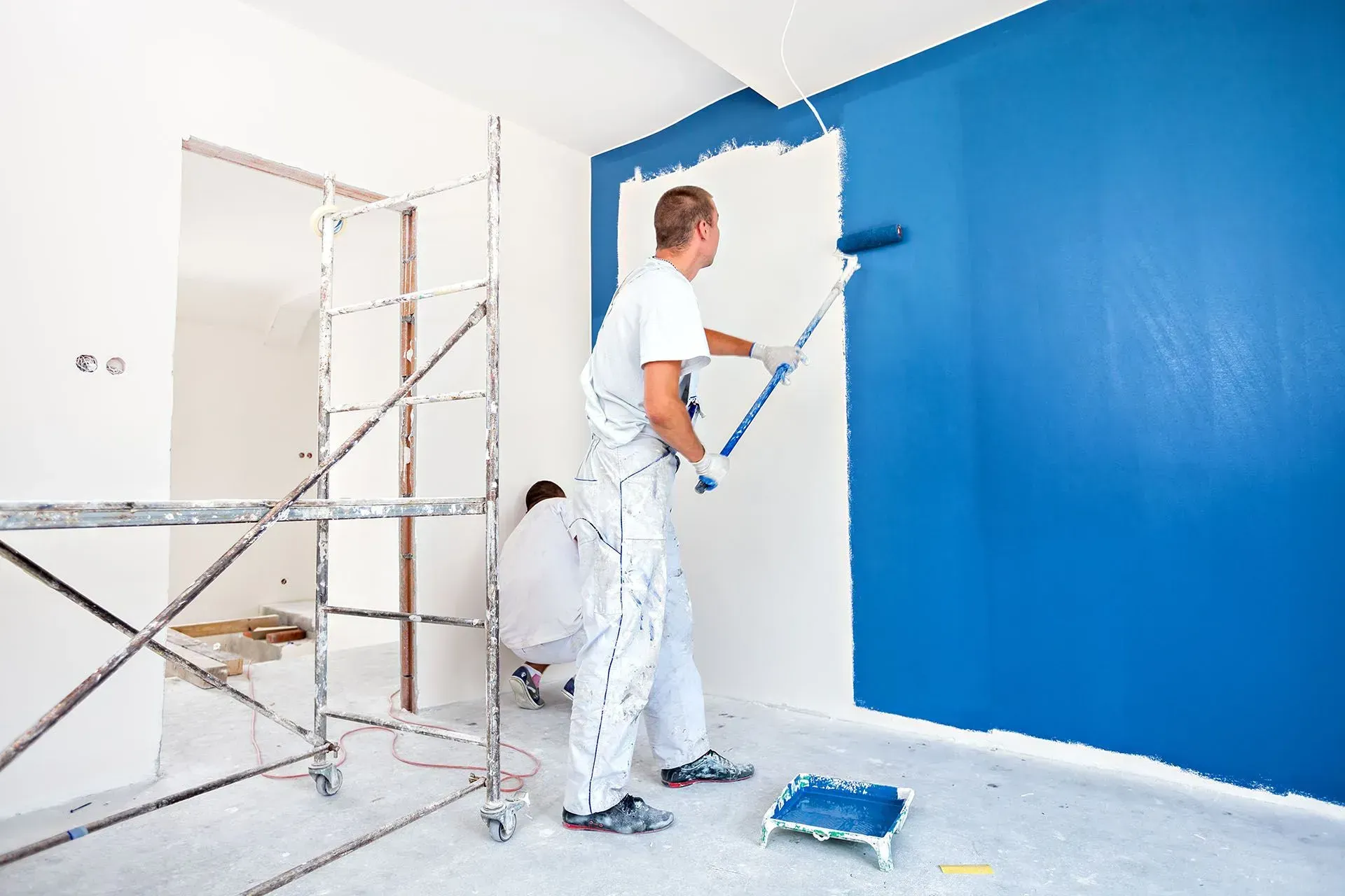 Two men are painting a wall blue and white.