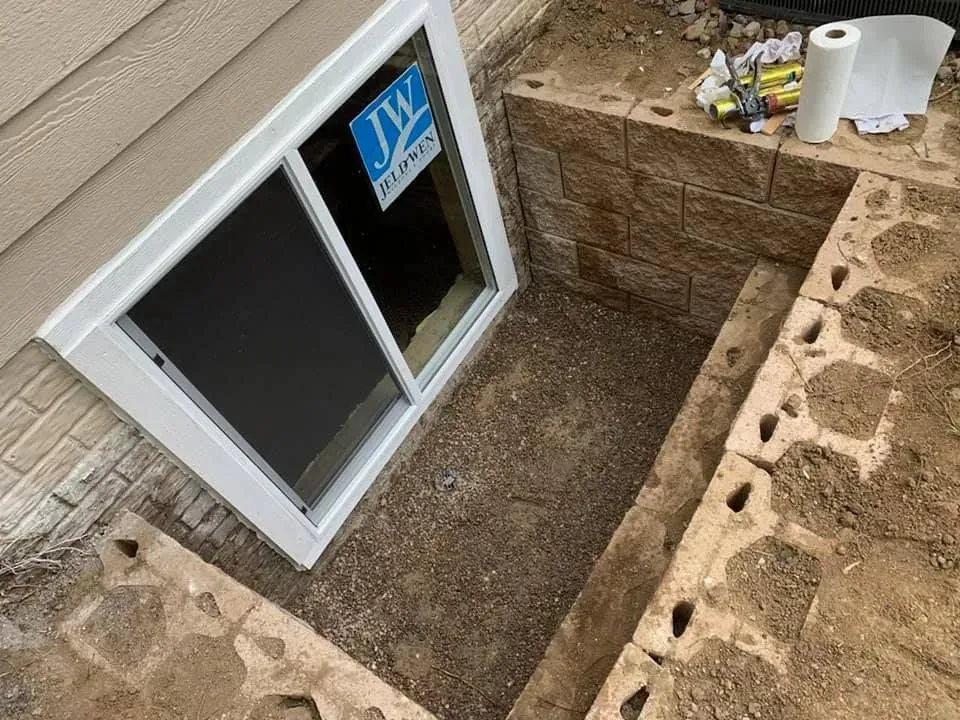 A window is being installed in a basement next to a brick wall.