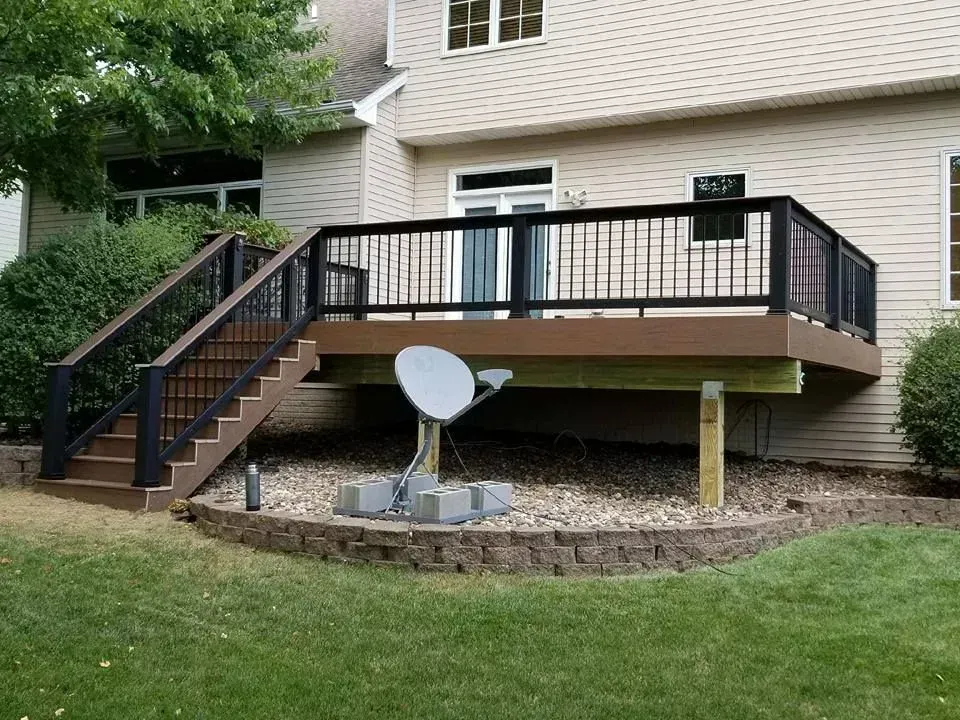 A deck with stairs and a satellite dish on it in front of a house.