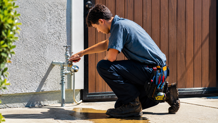 Technician in red jacket and gloves working on copper pipes with a wrench inside a utility room