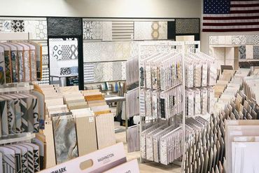Tile showroom with various tile samples displayed on walls and shelving, American flag in the background.