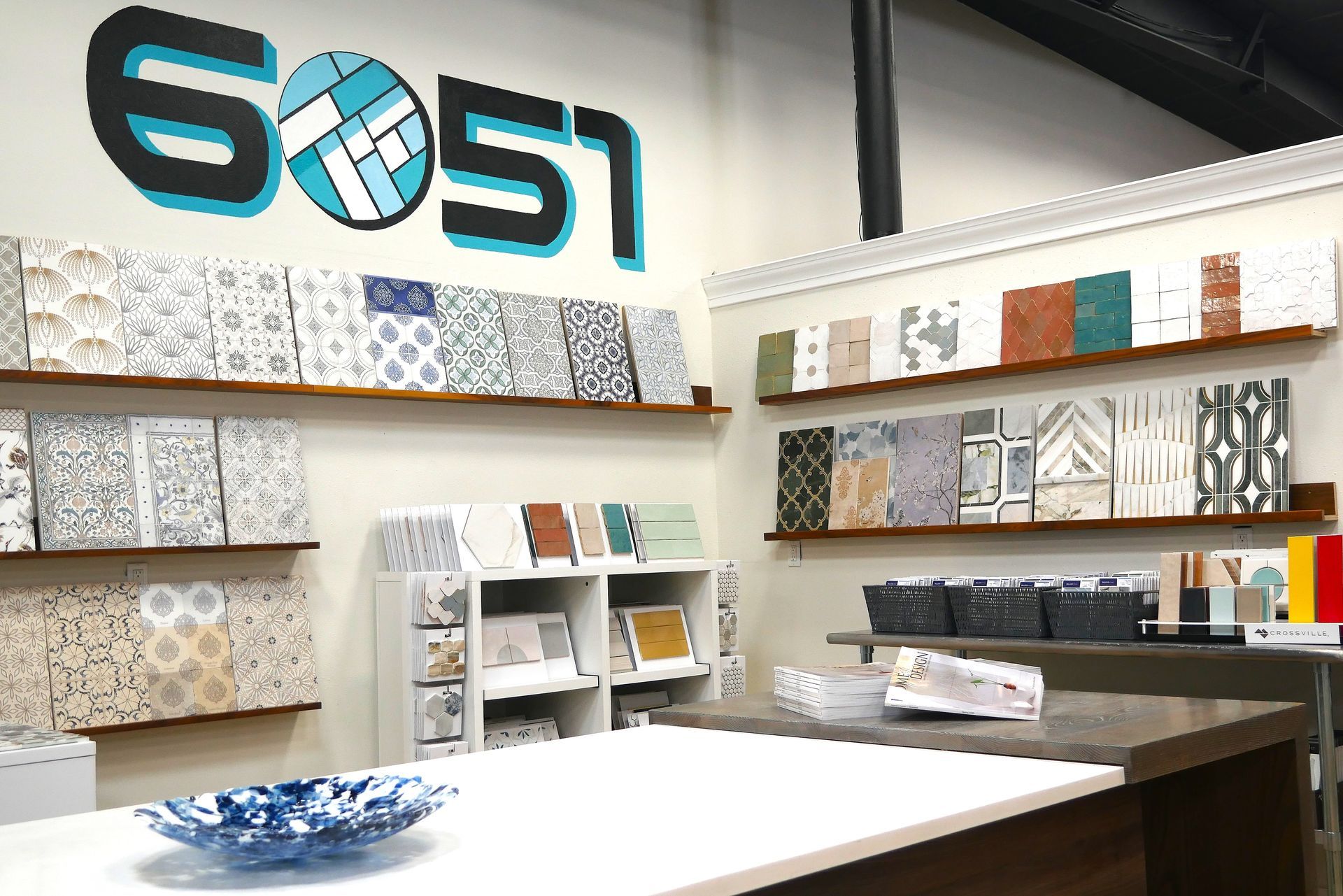 Interior shot of a tile showroom with various tile samples displayed on shelves. The business logo 
