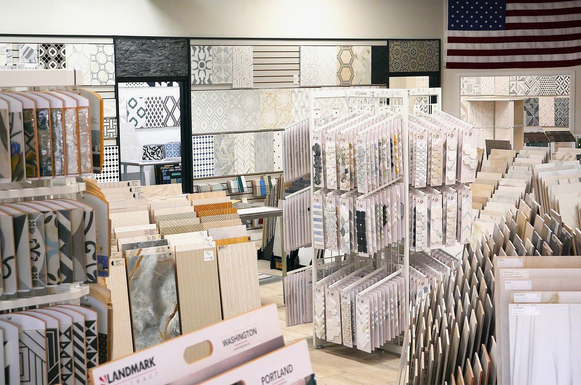 Tile showroom with a wide variety of tile samples displayed on racks and walls. An American flag hangs in the background.