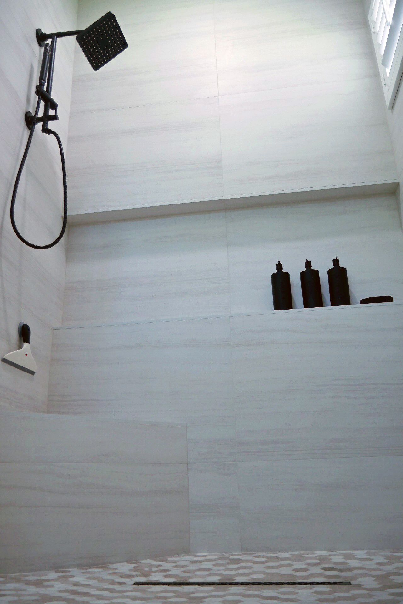 A bathroom with a shower head and a shelf with bottles on it