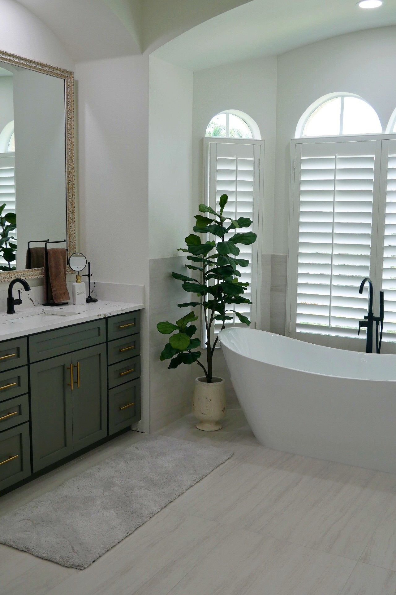 A bathroom with a tub, sink, mirror and shutters
