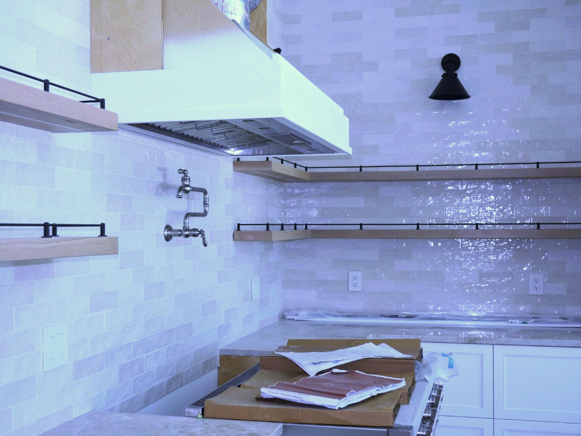 A kitchen with a stove top oven, shelves, and a hood
