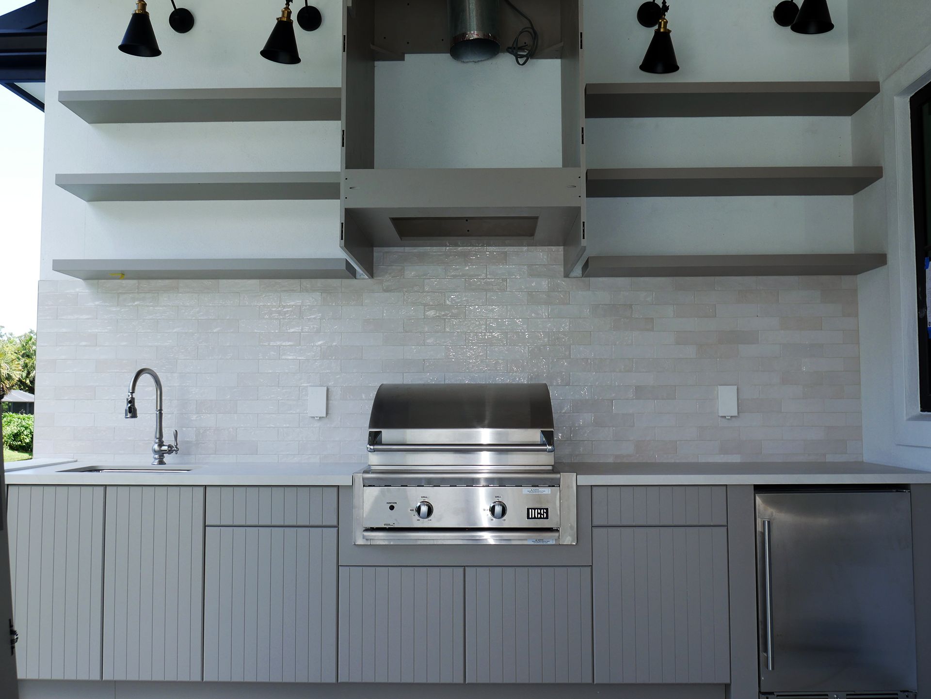 An outdoor kitchen with a grill, sink, and shelves