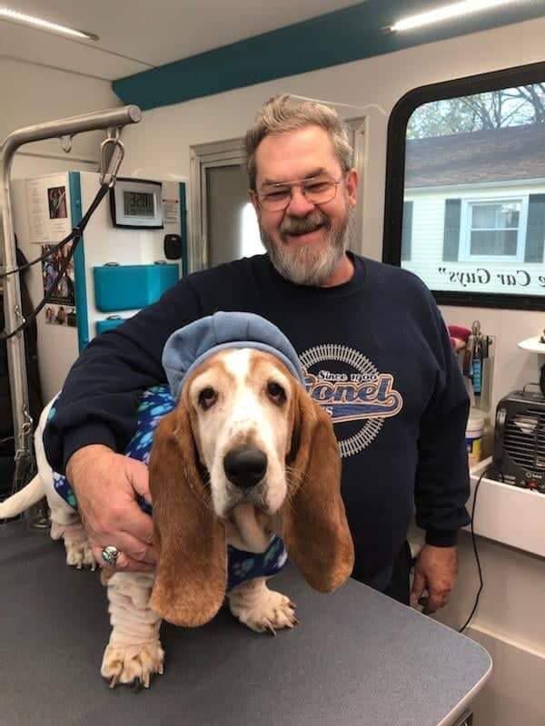 A man is holding a basset hound wearing a blue hat