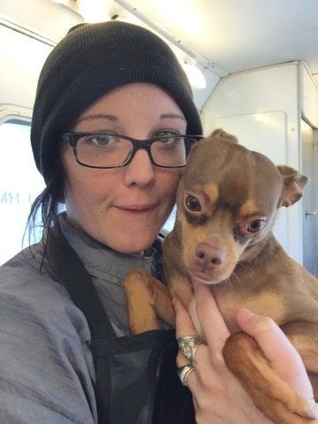 A woman is holding a small brown dog in her arms.