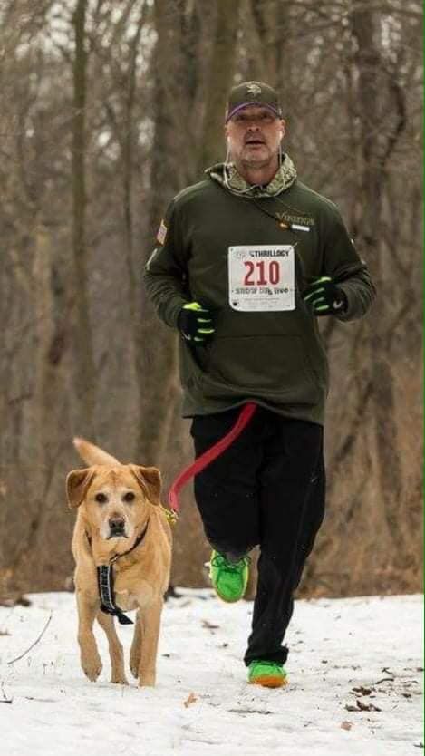 A man is running with a dog on a leash in the snow.