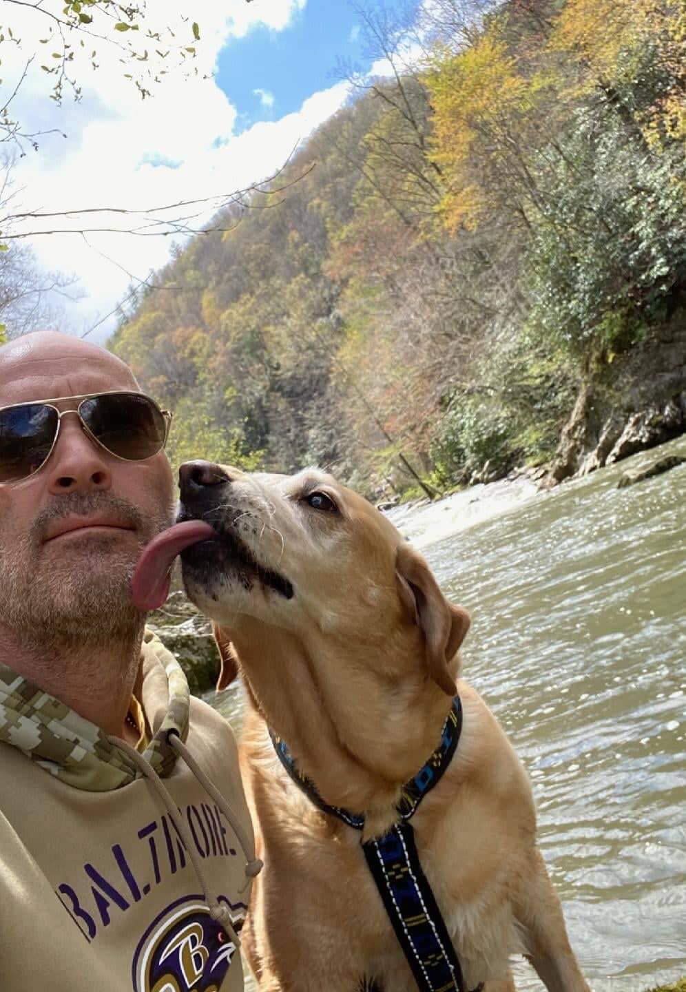 A man and his dog are standing next to a river.