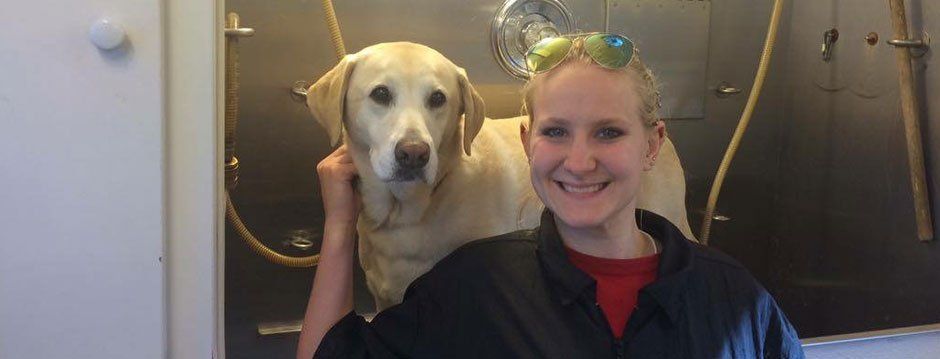 A woman is standing next to a dog in a shower.